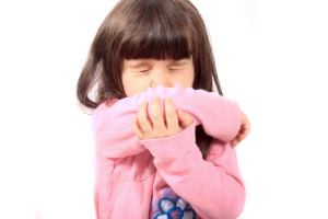 Little sick girl sneezing onto her sleeve because of sickness or allergies